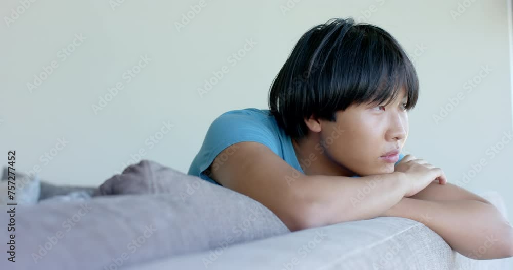 Teenage Asian boy with black hair looks pensive, resting his chin on his hands Teenage Asian boy with black hair looks pensive, resting his chin on his hands