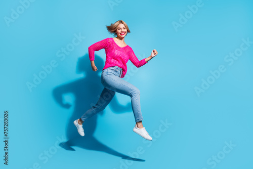 Full size photo of pretty young girl running fast have fun wear trendy pink knitwear outfit isolated on blue color background