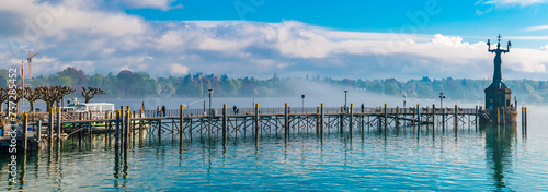 Lovely large panorama of the pier leading to the famous Imperia statue at the harbour entrance of Constance (Konstanz) by Lake Constance (Bodensee) in Germany on a spring day with blue sky.  photo