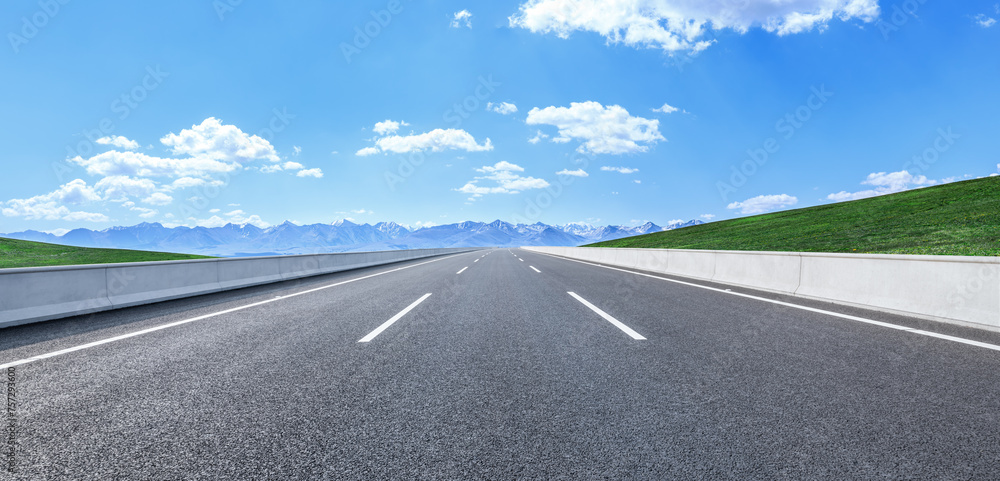 Asphalt highway road and green meadow with mountain nature landscape under blue sky Asphalt highway road and green meadow with mountain nature landscape under blue sky