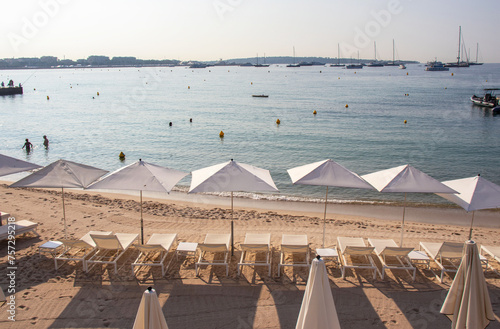 Rows of white umbrellas and sun loungers line the golden sandy beach in Cannes in the French Riviera in the early morning while a few swimmers and anglers have already started the day.