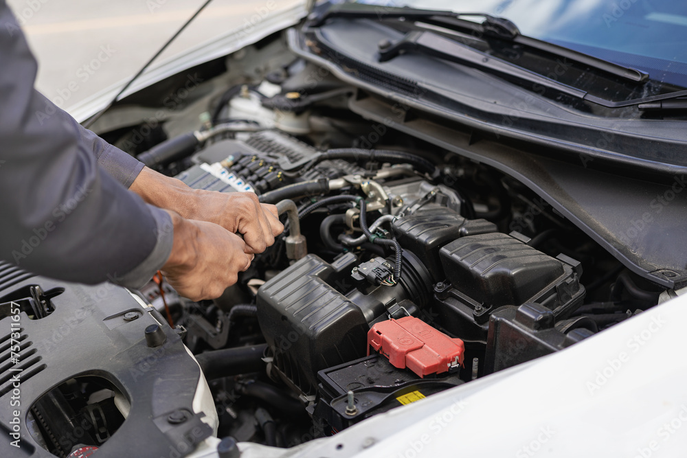 Auto mechanic looks under the hood of a broken car and checks the oil level on the side of the road. Car broken down on the side of the road, man trying to repair broken old car, car service concept Auto mechanic looks under the hood of a broken car and checks the oil level on the side of the road. Car broken down on the side of the road, man trying to repair broken old car, car service concept