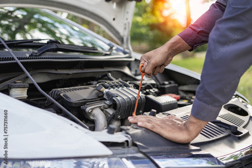 Auto mechanic looks under the hood of a broken car and checks the oil level on the side of the road. Car broken down on the side of the road, man trying to repair broken old car, car service concept Auto mechanic looks under the hood of a broken car and checks the oil level on the side of the road. Car broken down on the side of the road, man trying to repair broken old car, car service concept