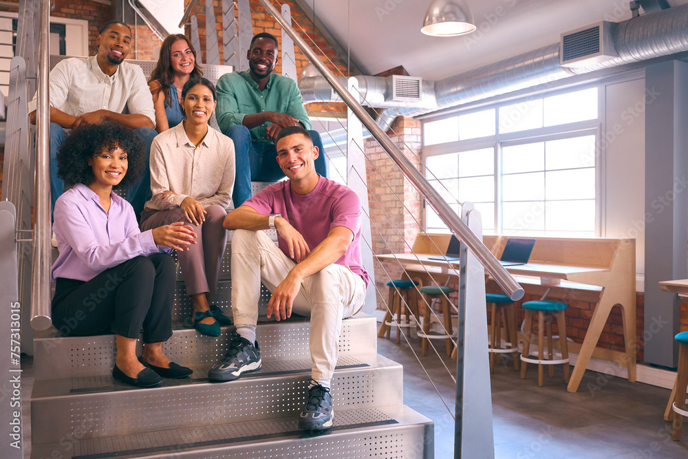 Portrait Of Smiling Multi-Cultural Business Team Sitting On Stairs In Modern Open Plan Office 