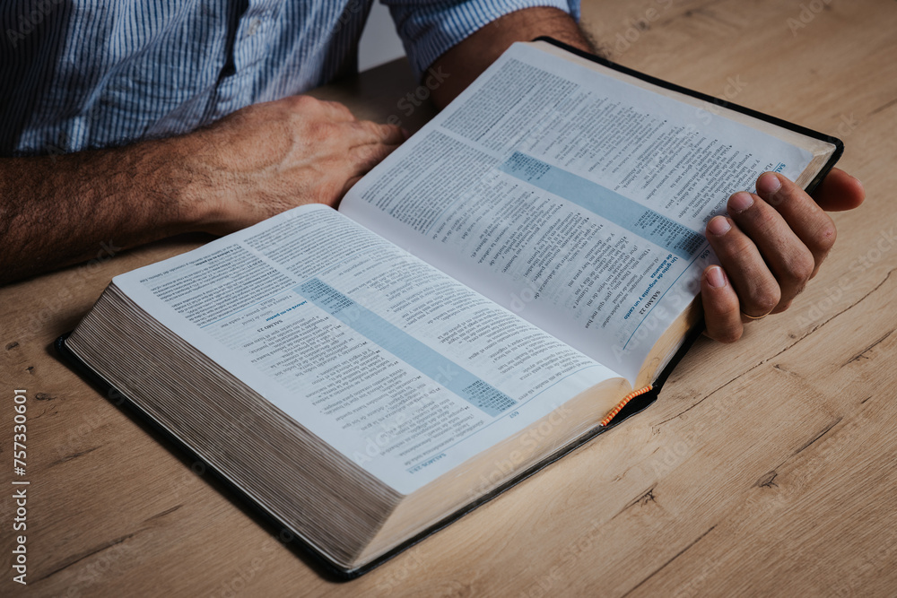 Naklejka premium Man is reading the bible, holding with his hand the holy book, in a low-light environment