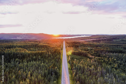 Sonnenuntergang über weitem Wald mit gerader Straße in Skandinavien Roadmap Drohne