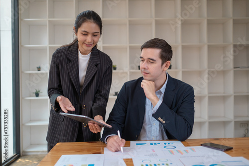 Two business people using a laptop ipad togerher in an office, a man and a women analyzing documents stat at office photo