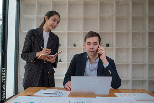 Two business people using a laptop ipad togerher in an office, a man and a women analyzing documents stat at office photo