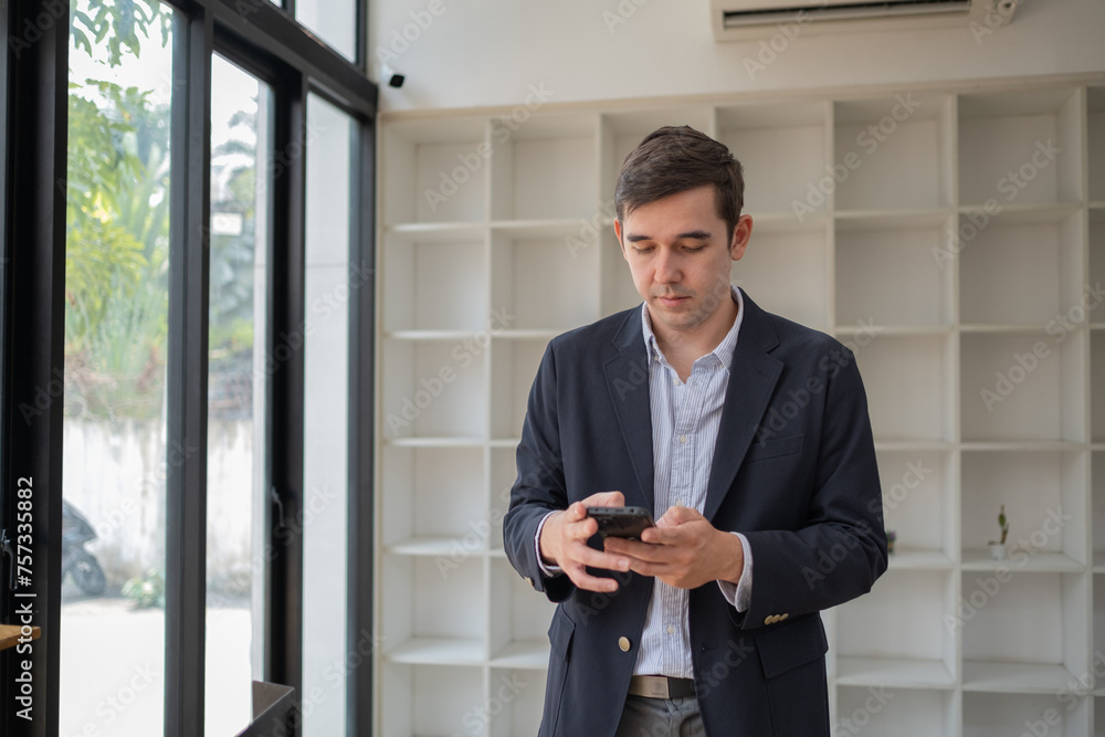 Happy business man talking on mobile cell phone device looking away standing at work, handsome businessman talking on his phone in office Happy business man talking on mobile cell phone device looking away standing at work, handsome businessman talking on his phone in office