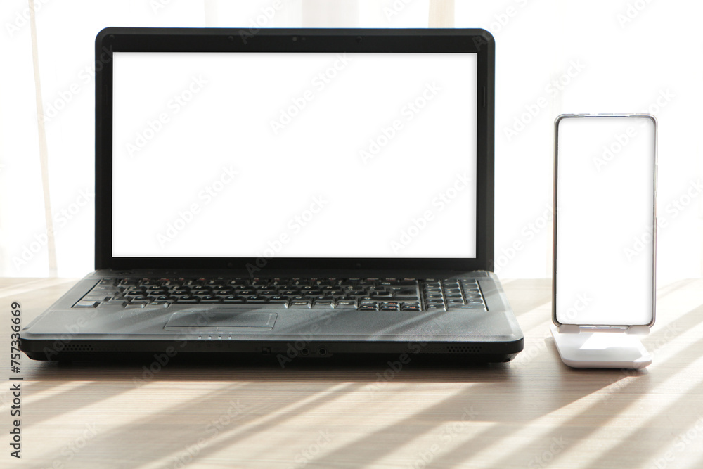 Laptop and smart phone with blank white screen. Smart phone in phone holder. mobile phone with stand holder on the desk. Mock up Laptop and smart phone with blank white screen. Smart phone in phone holder. mobile phone with stand holder on the desk. Mock up
