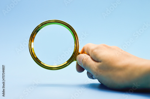 Male hand holding a magnifying glass blue background