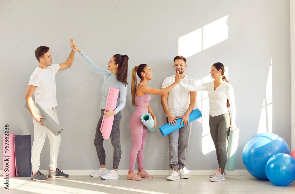 Naklejka premium Happy cheerful sporty people giving high five each other rejoicing the success in fitness after sport training in gym. Smiling men and women standing at the end of workout and talking.