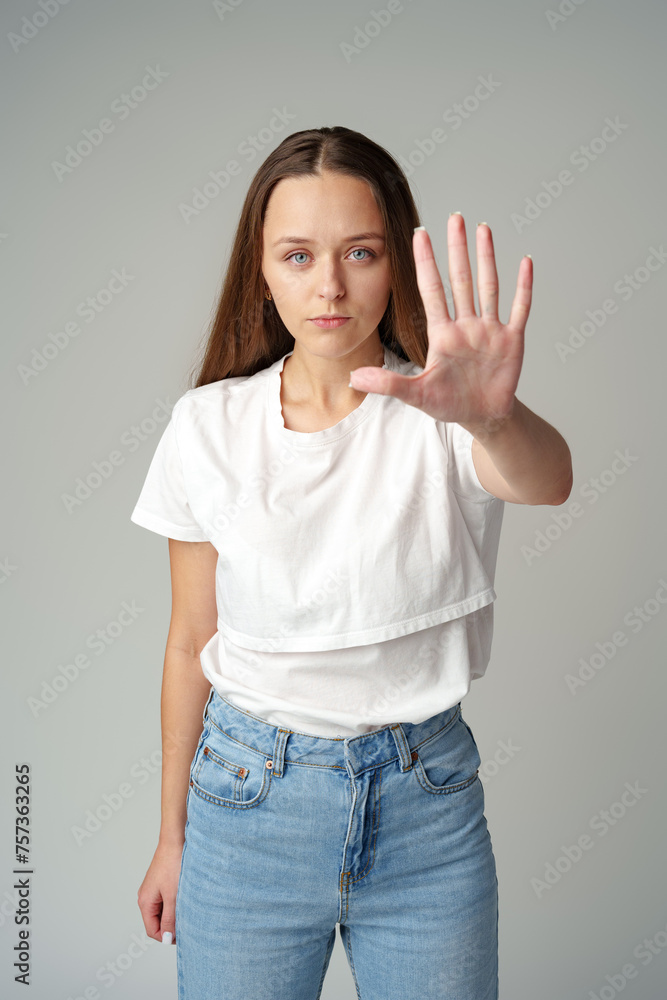 Portrait of a young woman standing with outstretched hand showing stop gesture on gray background Portrait of a young woman standing with outstretched hand showing stop gesture on gray background