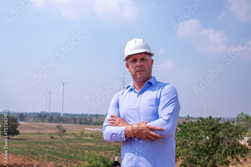 Engineer surveyor and manager wearing uniform walking holding box inspection and tablet work in wind turbine farms rotation to electricity, alternative renewable energy for clean power energy concept. photo