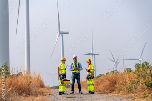 Engineer surveyor and manager wearing uniform walking holding box inspection and tablet work in wind turbine farms rotation to electricity, alternative renewable energy for clean power energy concept.