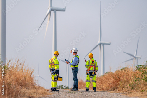 Engineer surveyor and manager wearing uniform walking holding box inspection and tablet work in wind turbine farms rotation to electricity, alternative renewable energy for clean power energy concept.