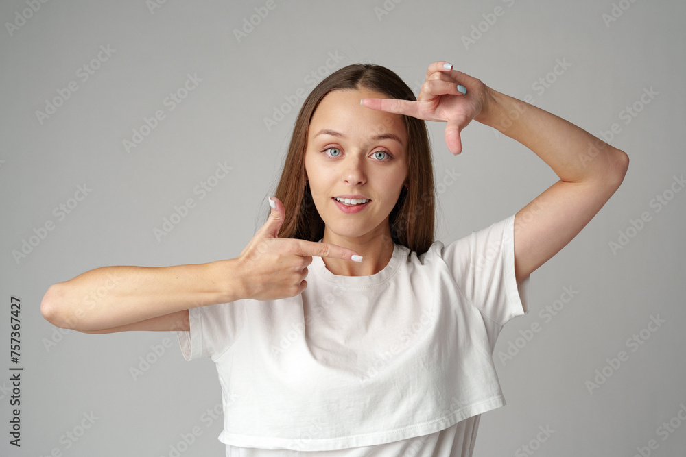 Young woman making frame with fingers on a gray background Young woman making frame with fingers on a gray background