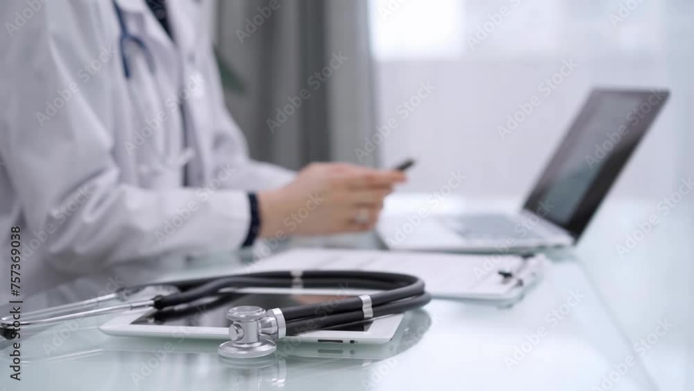 Stethoscope and medical clipboard are lying on the glass table while doctor woman is working with laptop computer on the background. Medicine and pharmacy concept Stethoscope and medical clipboard are lying on the glass table while doctor woman is working with laptop computer on the background. Medicine and pharmacy concept