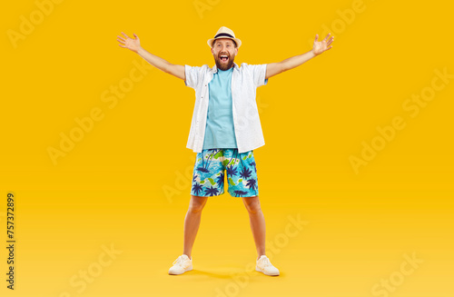 Cheerful funny man in beach clothes with outstretched arms is glad to see you at summer resort. Portrait of joyful playful guy in shorts, t-shirt, shirt and panama having fun on orange background.