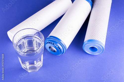 set three of cartridges for water filter with clear glass of water isolated on violet background. Concept of water treatment technology. filter cartridges to domestic water treatment systems.