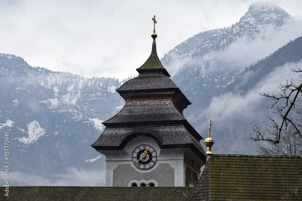 Fototapeta premium Torre de iglesia parroquial con reloj y las montañas nevadas de fondo