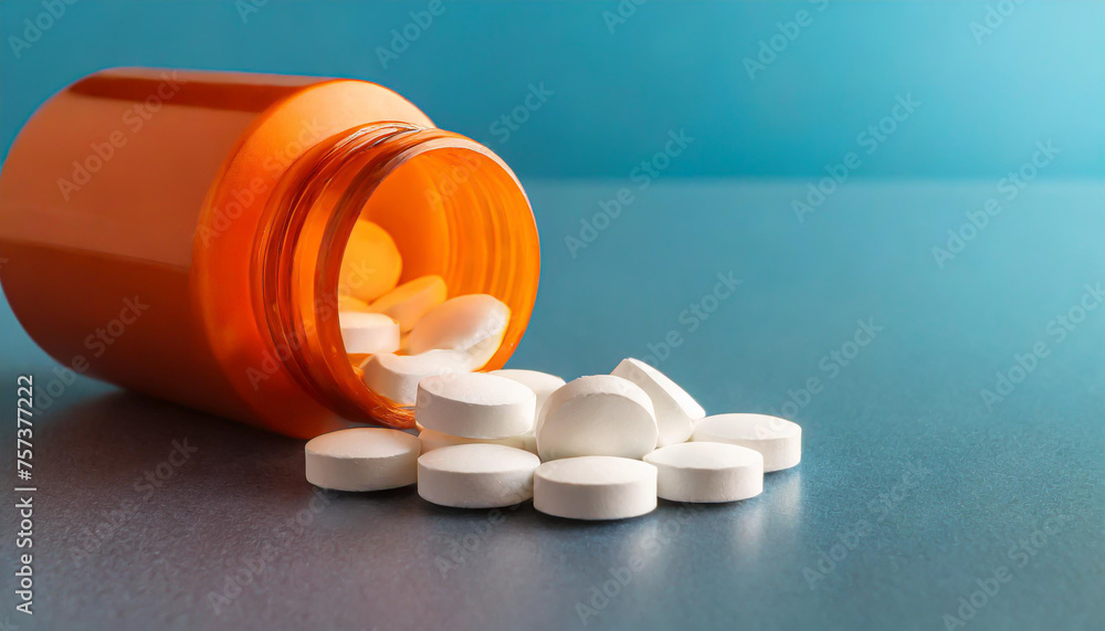 White pills in orange bottle on blue background close up with copy space White pills in orange bottle on blue background close up with copy space