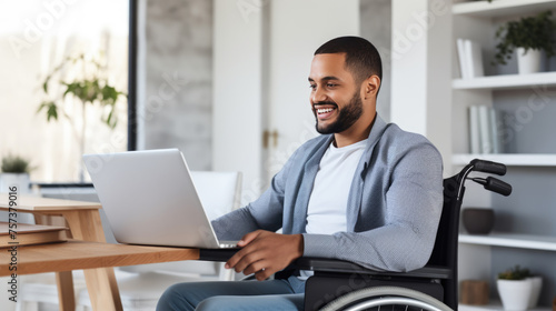 Smiling man in a wheelchair works on laptop in his home office.