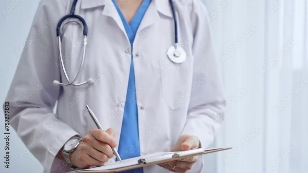 Female doctor taking notes on clipboard. Close-up of a unrecognizable female healthcare professional writing and filling um medication history records form while standing straight in clinic