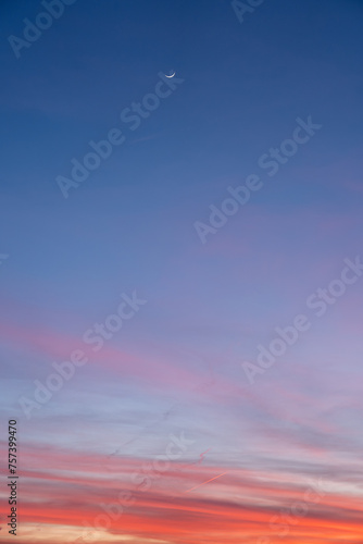 Sunset over the clouds with crescent moon and a plane.