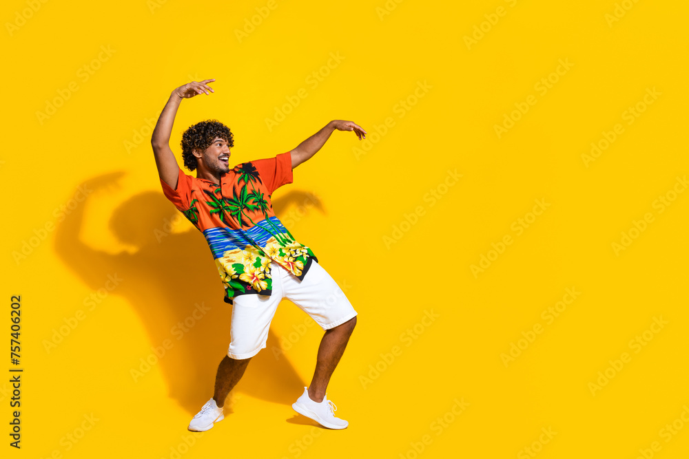 Full length photo of optimistic guy wear hawaii print shirt hold arms up look at discount empty space isolated on yellow color background