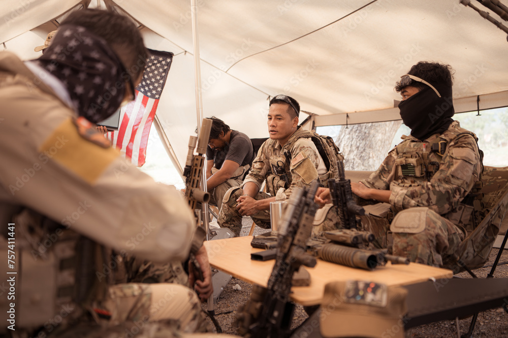 Group of soldiers in camouflage uniforms hold weapons in a field tent, Plan and prepare for combat training. Group of soldiers in camouflage uniforms hold weapons in a field tent, Plan and prepare for combat training.