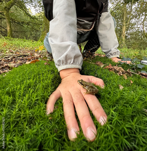 Child shows gesture of holding small frog in hand on grassland