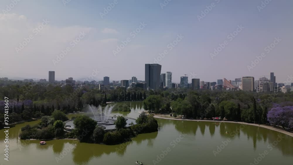 Drone over a lake at Chapultepec park in Mexico City revealing a fountain and skyline Drone over a lake at Chapultepec park in Mexico City revealing a fountain and skyline