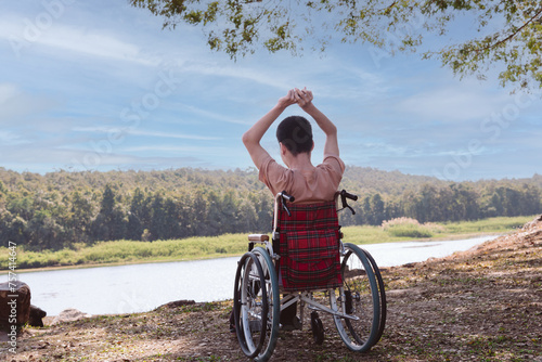 Back of young boy sitting on wheelchair looking at beautiful nature park, Traveling using a wheel chair to learn about the world without limits, Good mental health and travel concept.