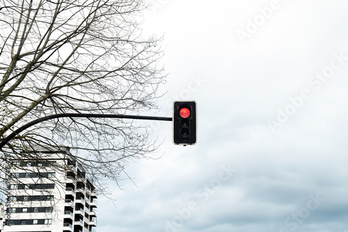 Red Traffic Light Against Cloudy Sky and Bare Tree photo