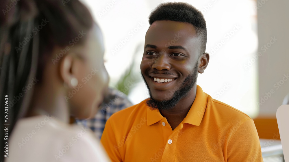 Beaming young man in an orange shirt shares a joyful conversation in a luminous setting.