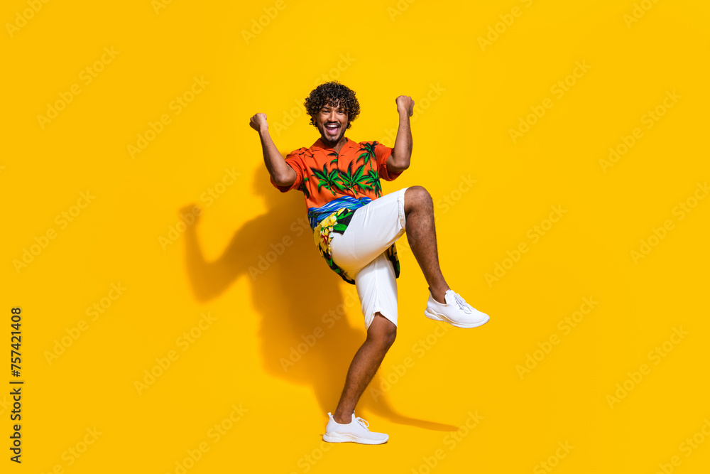 Full length photo of optimistic guy wear hawaii print shirt raising fists up win bet shout yes isolated on yellow color background
