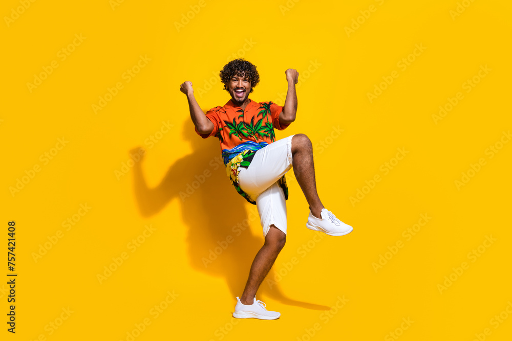 Full length photo of optimistic guy wear hawaii print shirt raising fists up win bet shout yes isolated on yellow color background Full length photo of optimistic guy wear hawaii print shirt raising fists up win bet shout yes isolated on yellow color background