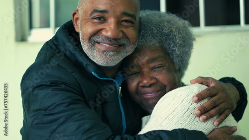 Adult South American black middle-aged son embracing elderly 80s gray-hair mother in loving tender hug depicting care and support in old age