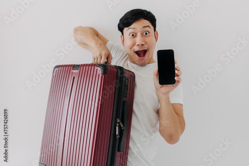 Wow face Asian man holds up a suitcase and a cell phone. He seems to be ready to travel with his mobile application.