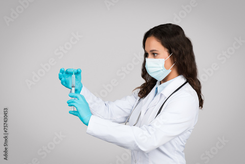 Vaccination concept. Doctor woman in protective medical mask looking at syringe  physician lady ready to make injection
