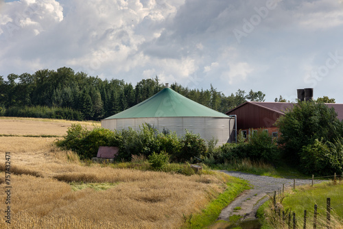 A large green dome tent sits in a field next to a barn