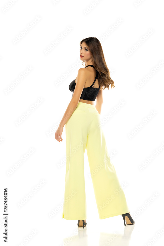 Fashion model posing in black blouse, yellow loose pants and high heel shoes. Rear view on a white background Fashion model posing in black blouse, yellow loose pants and high heel shoes. Rear view on a white background