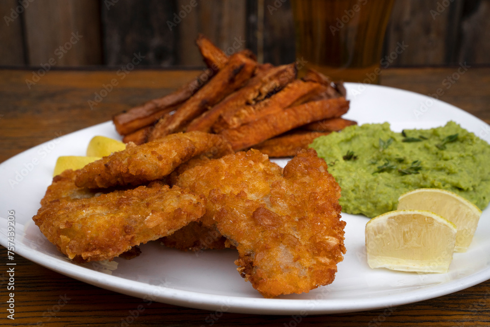 Closeup view of fried hake fillet with lemon, fried sweet potatoes and beans puree in a white plate with a wooden background. Closeup view of fried hake fillet with lemon, fried sweet potatoes and beans puree in a white plate with a wooden background.