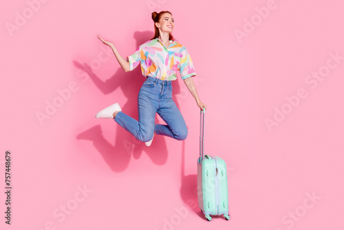 Full size photo of attractive girl colorful blouse jump hold suitcase palm hold offer look empty space isolated on pink color background
