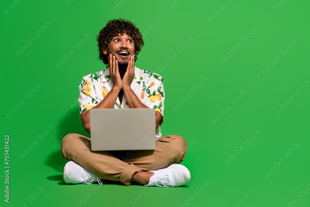 Full size photo of young male netbook look excited empty space dressed stylish citrus print outfit isolated on green color background Full size photo of young male netbook look excited empty space dressed stylish citrus print outfit isolated on green color background