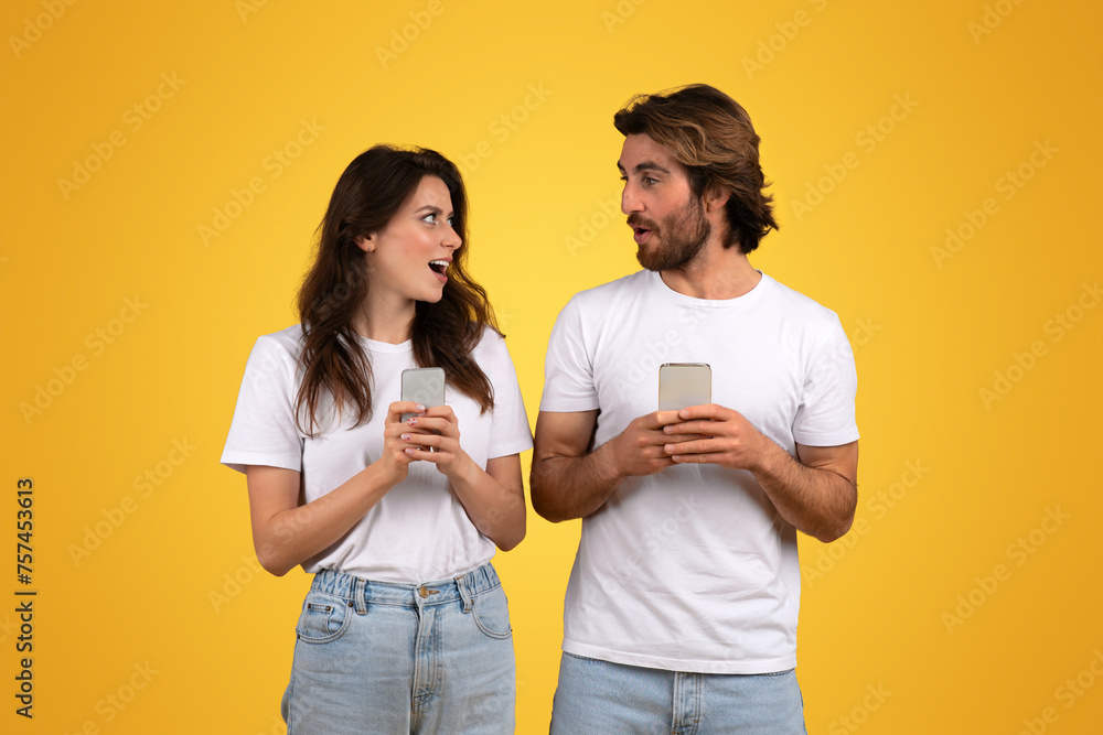 Engaged couple holding smartphones, the woman looking surprised and speaking to the man Engaged couple holding smartphones, the woman looking surprised and speaking to the man