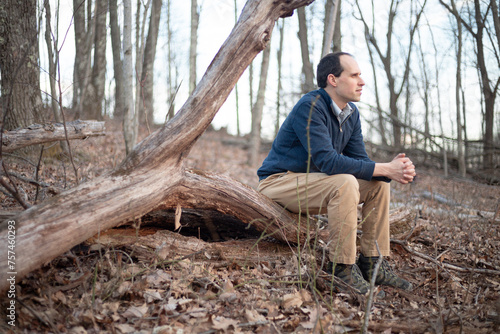 Man sitting on fallen tree in the woods gazing away