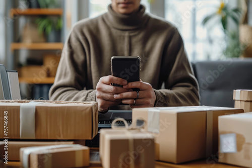 A person in a cozy sweater manages their online business, using a smartphone with shipping packages ready for dispatch on the table.