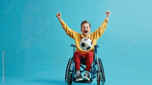 A stylish child in a wheelchair exudes joy, holding a football ball against a serene blue backdrop. Perfect for showcasing diversity in sports and youth empowerment photo